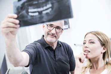 Zahnarzt zeigt dem Patienten, der im Zahnarztstuhl sitzt, ein Röntgenbild - FMKF002639