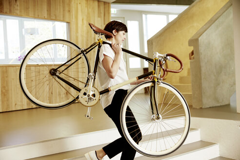 Woman carrying racing cycle on her shoulder in an office - TSFF000020