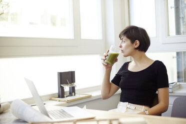 Porträt einer Frau, die im Büro einen grünen Smoothie trinkt - TSFF000042
