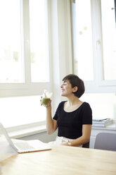 Glückliche Frau trinkt grünen Smoothie im Büro - TSFF000043