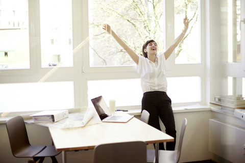 Lachende Frau bei Dehnungsübungen in ihrem Büro, lizenzfreies Stockfoto