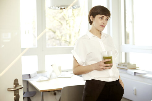 Tagträumende Frau mit einem Glas grünem Smoothie in einem Büro - TSFF000051