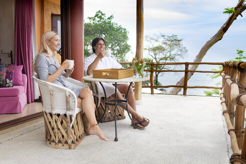 Happy couple sitting on terrace drinking coffee - ABAF002015
