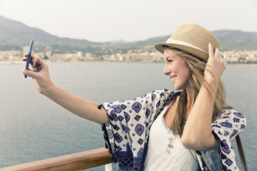 Lächelnde Frau auf einem Kreuzfahrtschiff, die ein Selfie mit ihrem Smartphone macht - ONBF000041