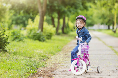 Lächelndes Mädchen auf Fahrrad mit Stützrädern - HAPF000489