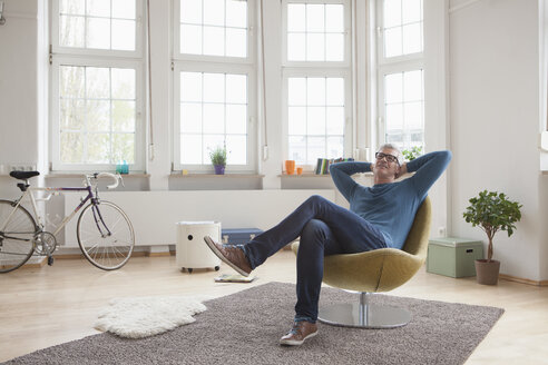 Entspannter reifer Mann zu Hause auf einem Stuhl sitzend - RBF004535