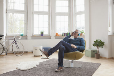 Relaxed mature man at home sitting in chair listening to music - RBF004537