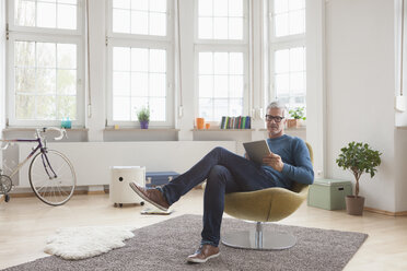 Mature man at home sitting in chair using digital tablet - RBF004538