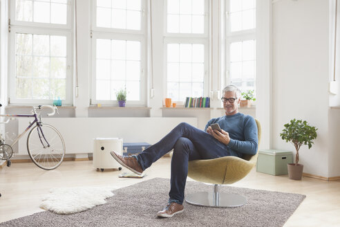 Älterer Mann sitzt zu Hause auf einem Stuhl und benutzt ein digitales Tablet - RBF004539