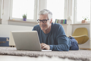 Älterer Mann zu Hause auf dem Boden liegend mit Laptop - RBF004542