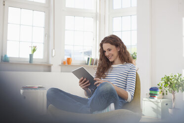 Woman at home sitting in chair using digital tablet - RBF004556