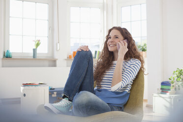 Woman at home sitting in chair talking on cell phone - RBF004557