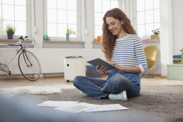 Woman at home sitting on floor using digital tablet - RBF004563