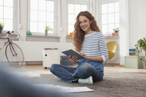 Woman at home sitting on floor using digital tablet stock photo