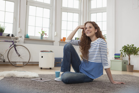 Lächelnde Frau zu Hause auf dem Boden sitzend, lizenzfreies Stockfoto