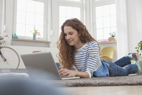 Woman at home lying on floor using laptop stock photo