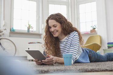 Frau zu Hause auf dem Boden liegend mit digitalem Tablet - RBF004570