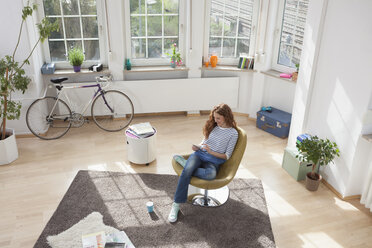 Woman at home sitting in chair using digital tablet - RBF004580