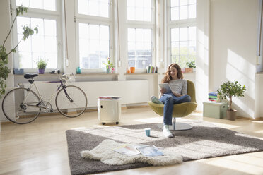 Woman at home sitting in chair using digital tablet - RBF004584