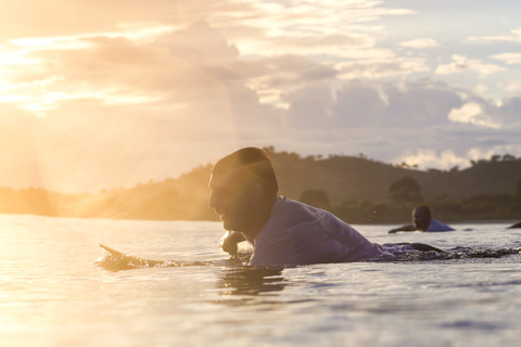 Indonesien, Insel Sumbawa, Surfer liegend auf Surfbrett am Abend, lizenzfreies Stockfoto