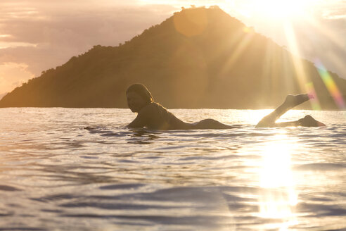 Indonesien, Insel Sumbawa, weibliche Surferin auf Surfbrett liegend am Abend - KNTF000288