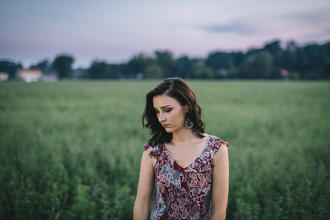 Portrait of a melancholic woman wearing a dress in a green field stock photo