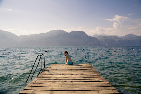 Italien, Brenzone, Mädchen sitzt auf Steg, lizenzfreies Stockfoto