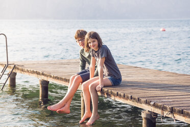 Brother and sister sitting side by side on jetty - LVF004909