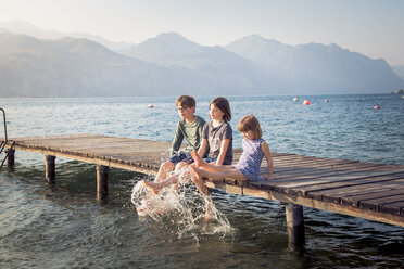 Italien, Brenzone, drei Kinder sitzen nebeneinander auf einem Steg und planschen mit Wasser - LVF004910