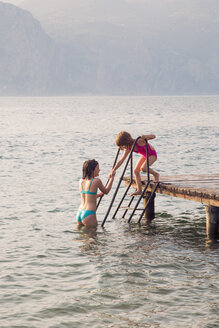 Italy, Brenzone, girl helping her little sister from jetty into the lake - LVF004915