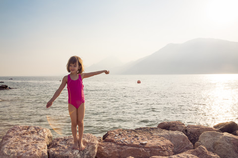 Italien, Brenzone, kleines Mädchen im Badeanzug, stehend am Seeufer, lizenzfreies Stockfoto