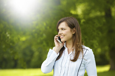 Smiling young woman telephoning with smartphone in a park - FMKF002712