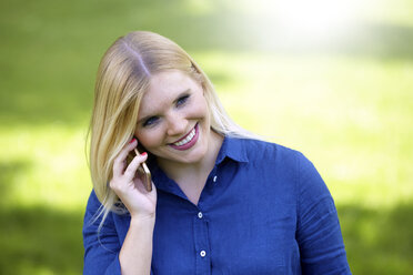Lächelnde junge Frau telefoniert mit Smartphone in einem Park - FMKF002714