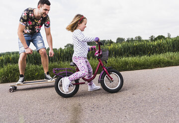 Father on skateboard accompanying daughter on bicycle - UUF007392