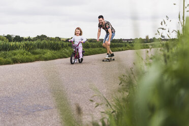 Vater auf Skateboard begleitet Tochter auf Fahrrad - UUF007393