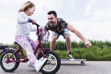 Father on skateboard accompanying daughter on bicycle - UUF007394