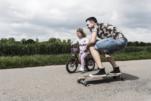 Father on skateboard accompanying daughter on bicycle - UUF007396