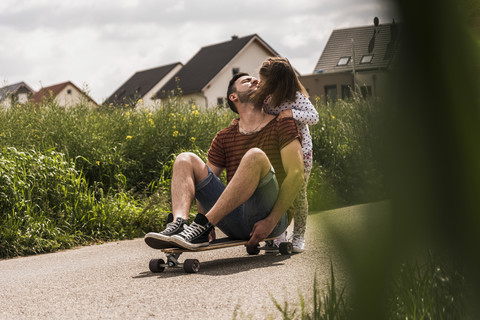 Tochter küsst Vater auf Skateboard, lizenzfreies Stockfoto