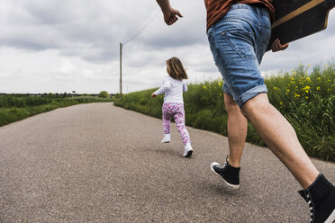 Vater mit Skateboard und Tochter läuft auf einem Feldweg - UUF007405