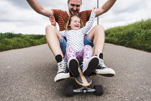 Tochter und Vater sitzen auf einem Skateboard - UUF007409