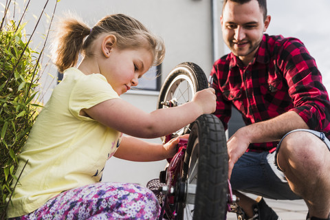 Vater und Tochter reparieren gemeinsam ein Fahrrad, lizenzfreies Stockfoto
