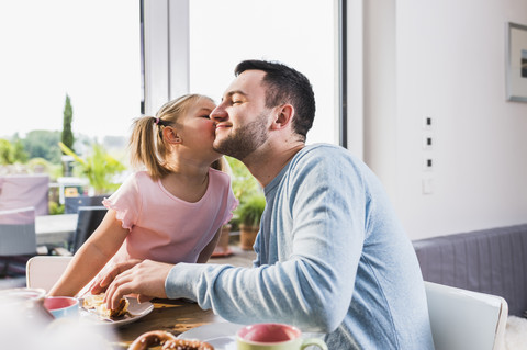 Tochter küsst Vater am Frühstückstisch, lizenzfreies Stockfoto