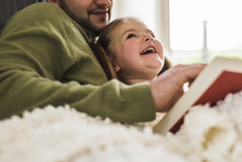 Glückliche Tochter schaut auf den Vater, der zu Hause ein Buch liest - UUF007454