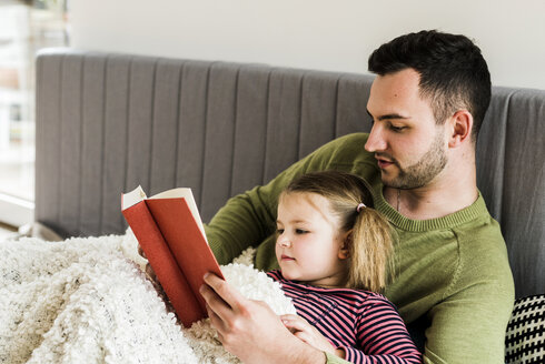 Vater und Tochter lesen zu Hause ein Buch - UUF007455