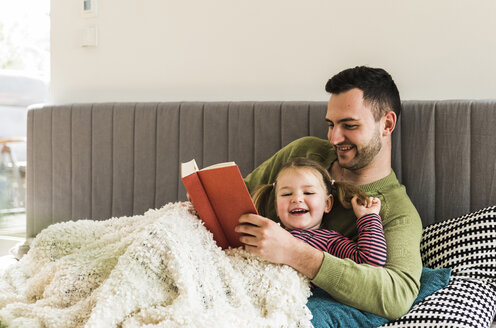 Happy father and daughter reading a book at home - UUF007456