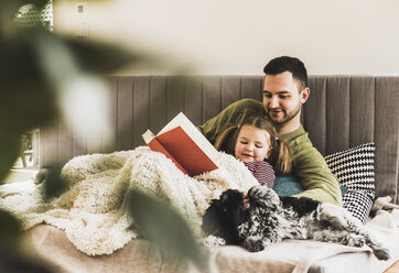 Vater und Tochter mit Hund lesen zu Hause ein Buch - UUF007457
