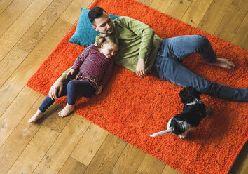 Father and daughter lying on carpet on the floor with dog - UUF007463