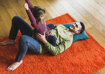 Verspielter Vater und Tochter liegen auf dem Teppich auf dem Boden - UUF007468