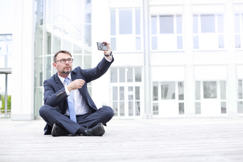 Geschäftsmann sitzt im Freien und macht ein Selfie, lizenzfreies Stockfoto