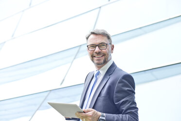 Lächelnder Geschäftsmann mit digitaler Tafel im Freien - MAEF011785